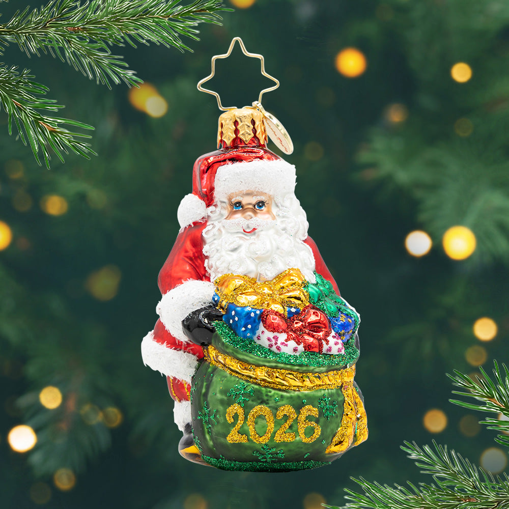 Santa's Yearly Gift Drop Gem. Ornament of Santa holding a green bag full of presents and the year 2026 in gold. View of front