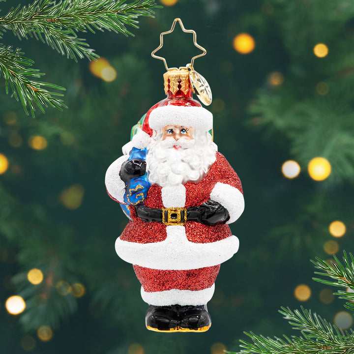 Jolly Old Kris Kringle Gem. Santa ornament in a sparkly red suit and holding a blue bag. View of front