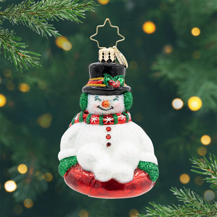 Snowy Slider Gem. Ornament of a snowman wearing a red and green scarf on a red sled. View of front