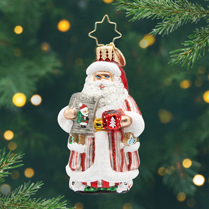 Santa's Daily News Gem. Ornament of Santa in a red and white striped pajama set while holding a list and a red mug. View of front