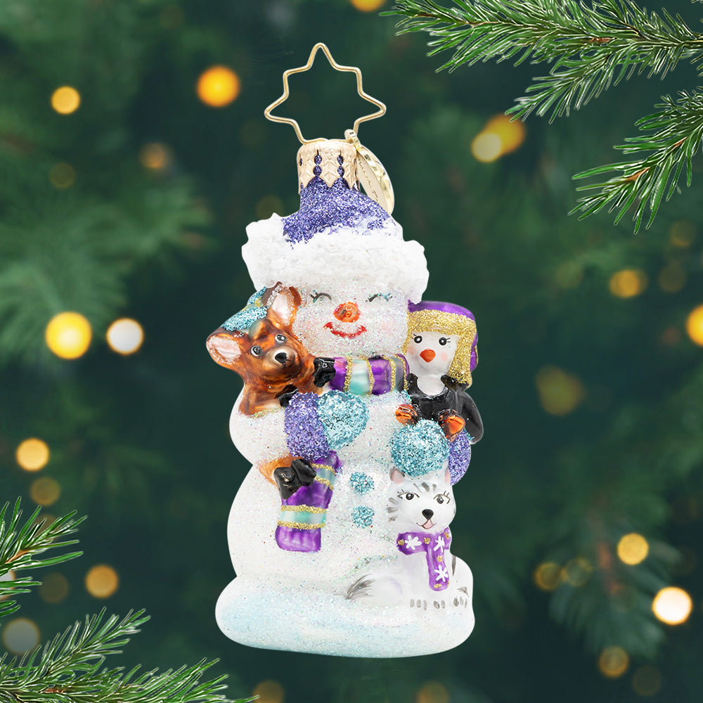 Snow Day Cuddles Gem. Snowman ornament in a purple scarf and hat holding a penguin, cat, and deer. View of front