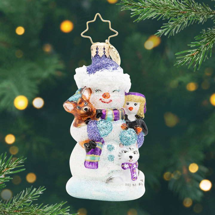 Snow Day Cuddles Gem. Snowman ornament in a purple scarf and hat holding a penguin, cat, and deer. View of front