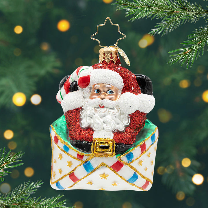 Letters to Santa Gem. Ornament of Santa in his classic sparkly red suit popping out of a white envelope with red, blue stripes and gold stars. View of front
