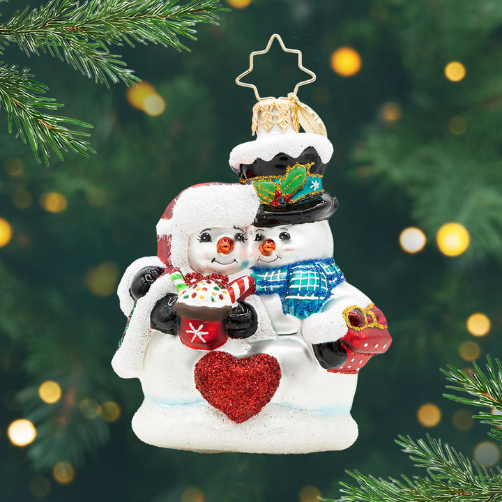 Winter Lovebirds Gem. Snow couple with one holding a hot chocolate, another a present and a red heart in the middle. View of front