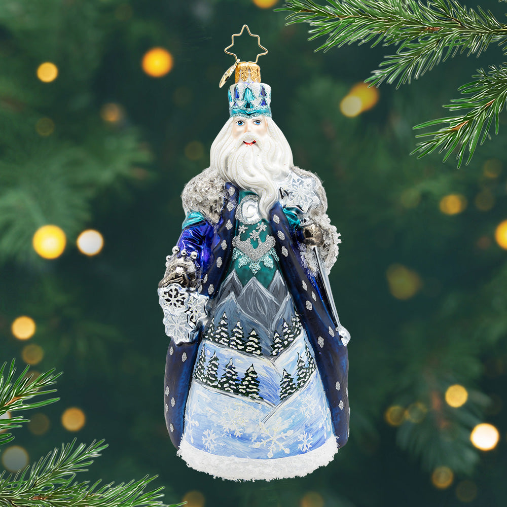 Frozen Majesty. Ornament of Santa in blue cloak with sparkling silver detailing's and a night scene of mountains and trees painted in the front. View of front.