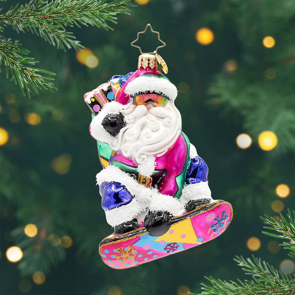Shreddin' Claus. Santa ornament in a neon snowsuit, rainbow goggles, and a graffiti-bright snowboard and a backpack full of presents. View of front.