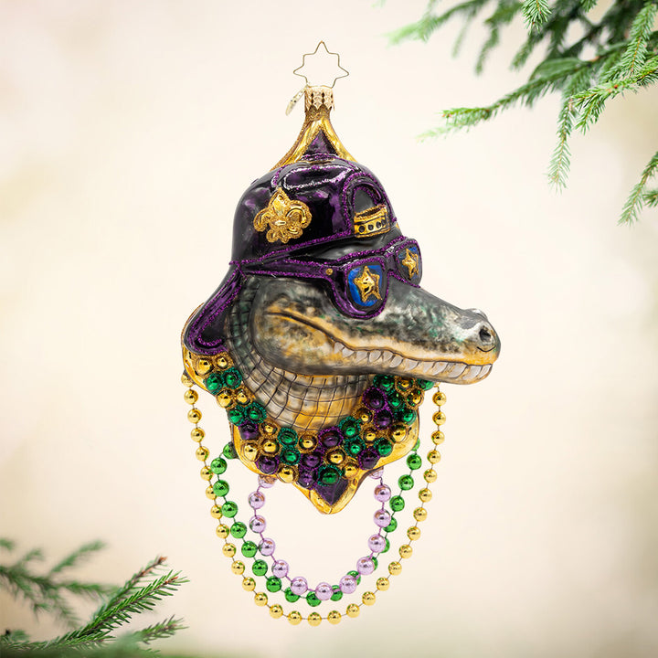 Gator Gras. Ornament. Alligator head wearing yellow, green, and purple beaded necklaces with a black and purple hat and glasses. View of front