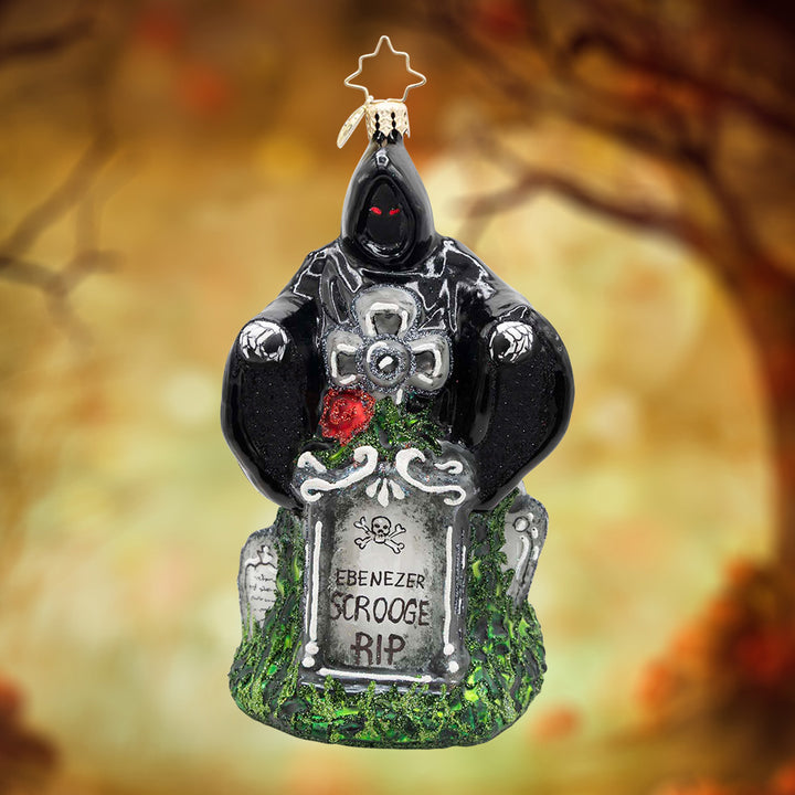 Ghost of Christmas Yet to Come. Ornament of Ghost of Yet to Come, dressed in a black cloke, standing behind a grey grave stone. View of front.