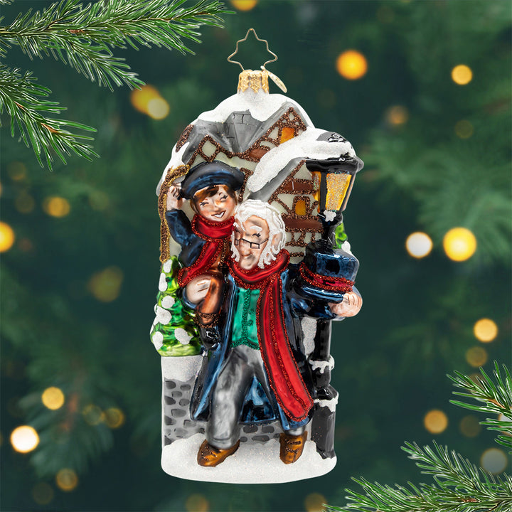 Scrooge’s Second Chance. Ornament of both Mr. and Mrs. Fezziwig dressed in blue coats and matching red scarves and blue hats while celebrating in front of a house. View of front