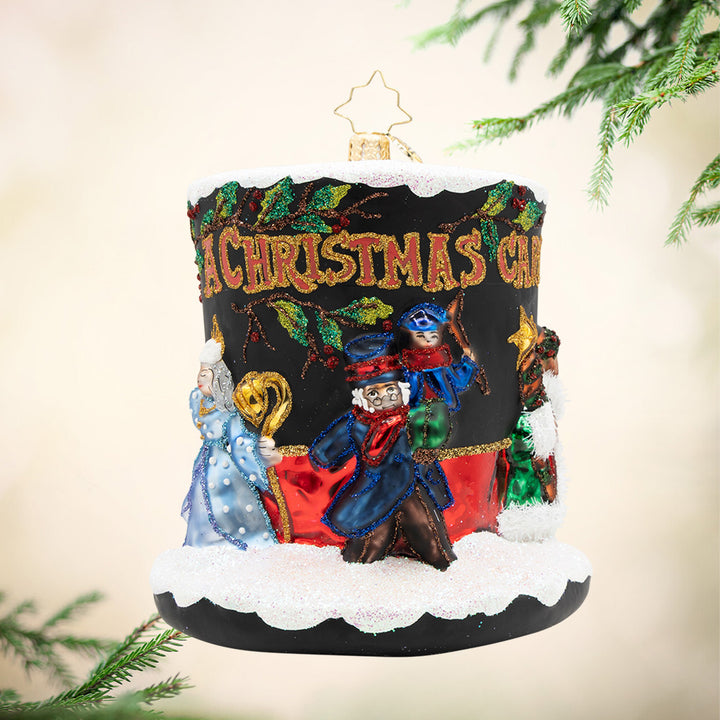 A Timeless Christmas Tale. A black top hat ornament covered in snow with the phrase "A Christmas Carol" in red and gold. Mr. Scrooge and the three ghosts also make an appearance around the hat. View of front