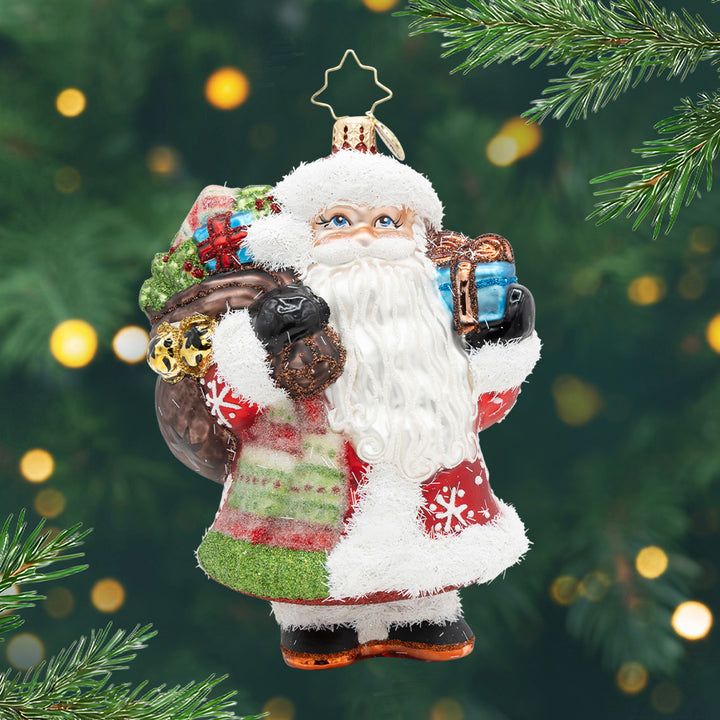 The Jolliest Fellow. Ornament of Santa carrying a brown bag full of presents in one hand and in the other a blue present. View of front