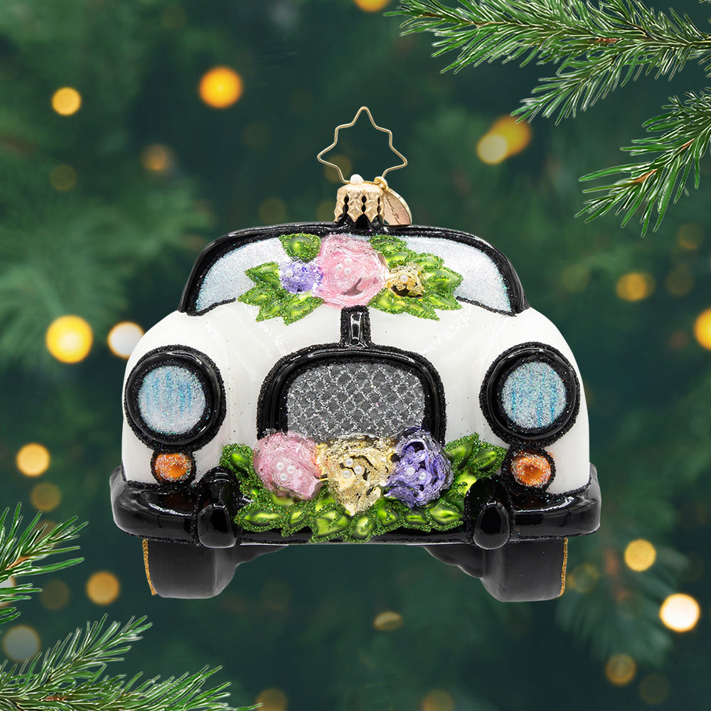 Sweetheart Getaway. Ornament of a white convertible, adorned with flowers, glitter-trimmed banners, and a cascade of soft florals. View of front.