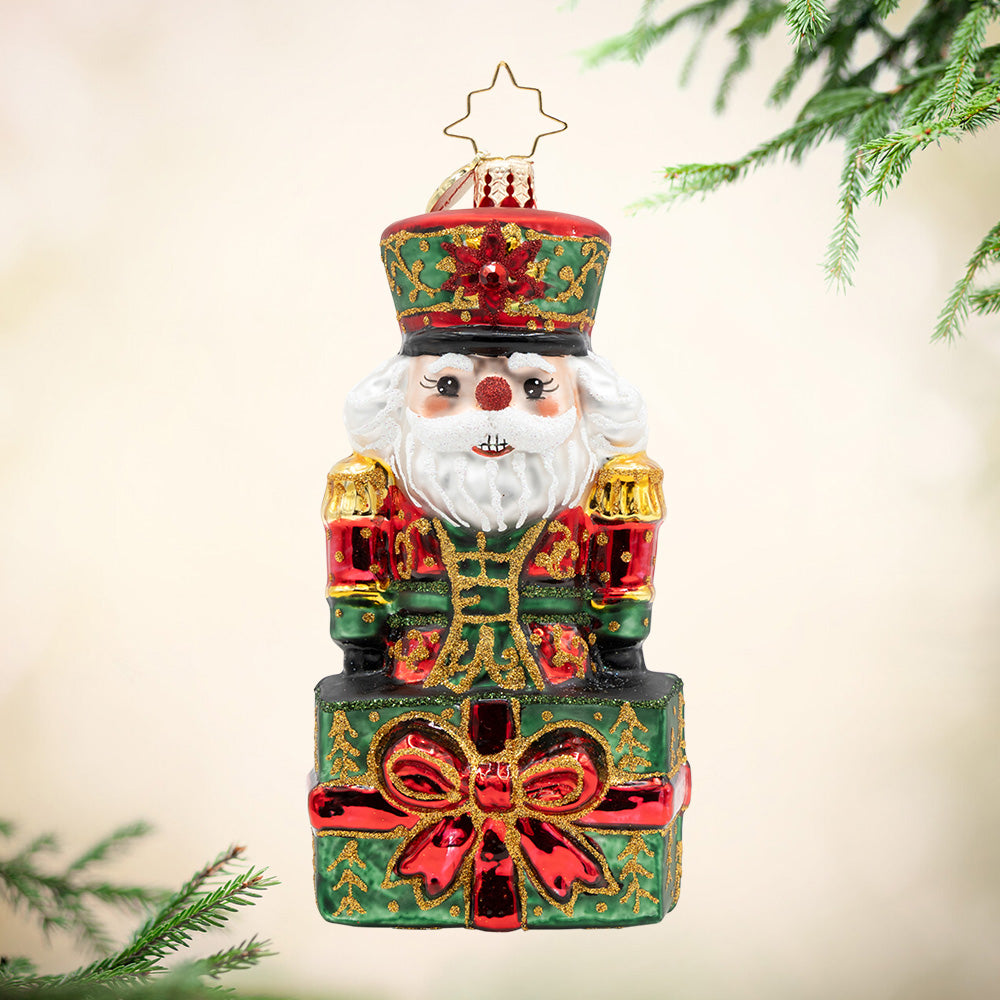 The Gifted Guard. Nutcracker ornament, in the colors red, green, and gold, popping out of a present. View of front