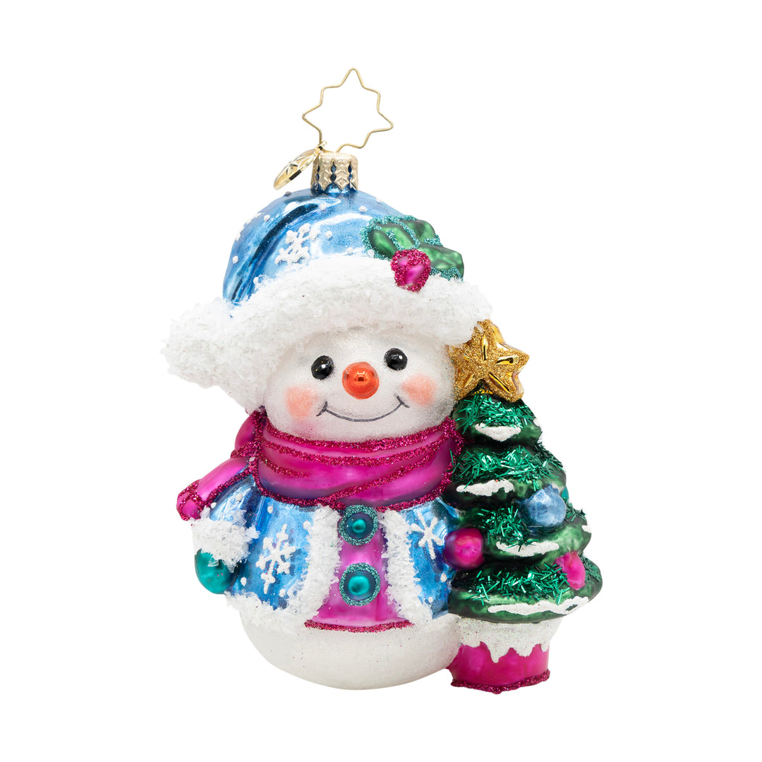 Frosted Flurries. Snowman ornament dressed in blue coat with a matching hat and a pink scarf, while standing next to a small Christmas tree. View of front