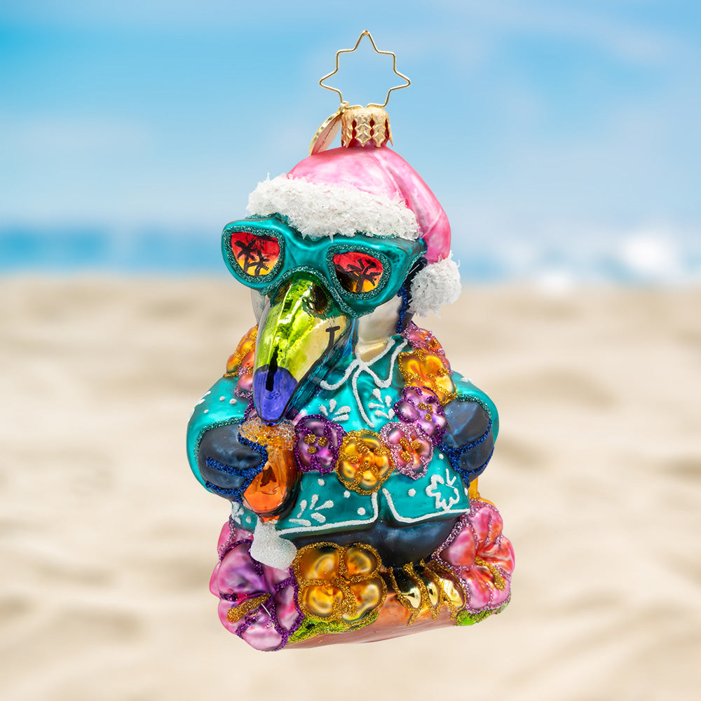 Toucan Tidings. Ornament of a toucan dressed in a blue tropical shirt with matching glasses while wearing a floral necklace and pink Santa hat. View of front