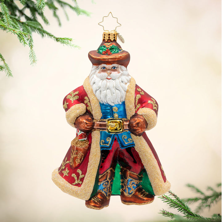 Decorative Santa Claus ornament with a red coat and white beard, standing against a light background with greenery.
