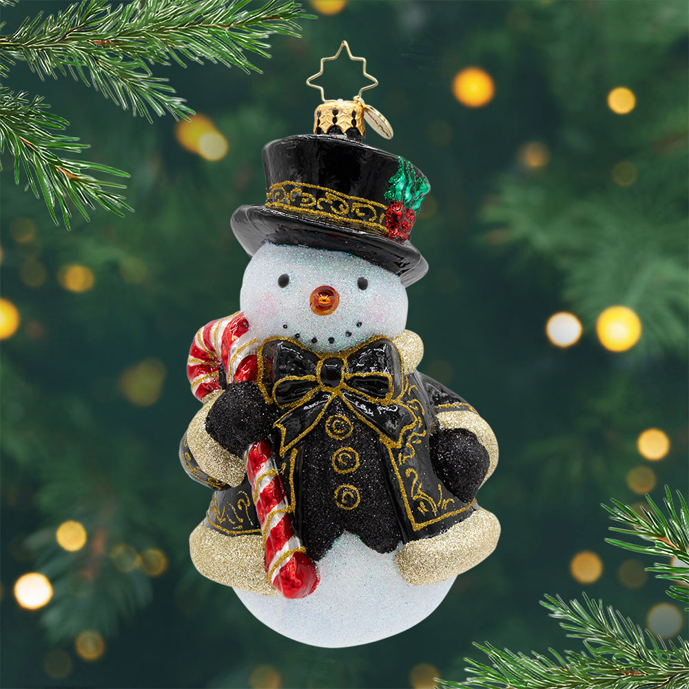 The Frosted Gentleman. A snowman ornament dressed in top hat, black coat with ornate gold trim, and a candy cane in hand. View of front.