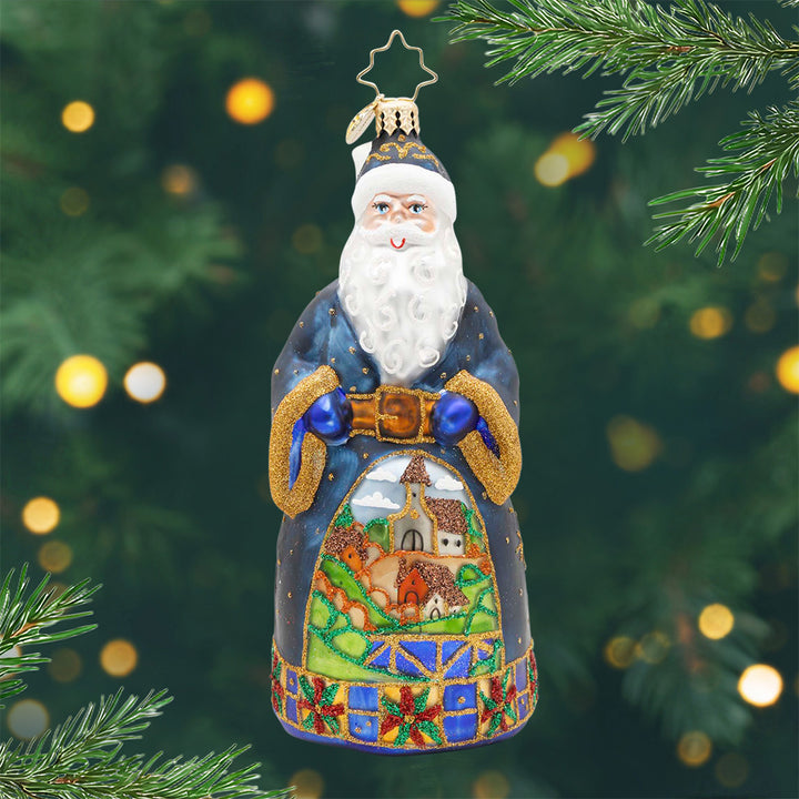 Santa's Keepsake Village. Ornament of Santa in a blue coat with a hand-painted village nestled among rolling hills. View of front