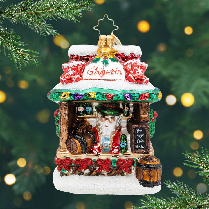 Glühwein Greetings. Ornament of a European market with Glühwein Greetings with Santa serving from the stand with frosty mugs, glittering bottles to tiny menu signage, and traditional Christmas details from top to bottom. View of front.
