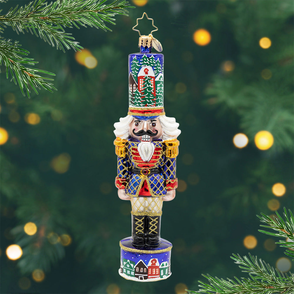 Christmas Sentinel. Nutcracker ornament in colors of blue, red, and green. with houses on its hat and base. View of front.