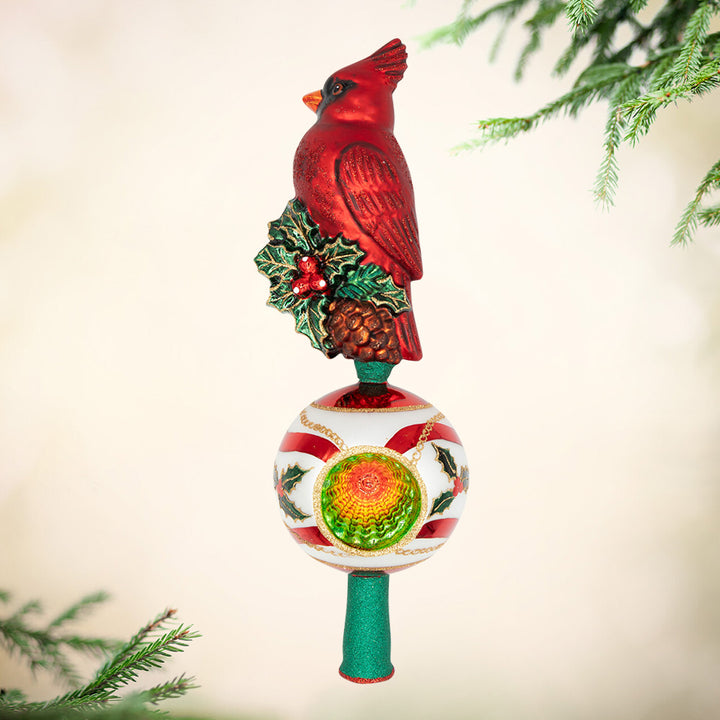 Majestic Cardinal Greetings Finial. Ornament of a bright red cardinal standing on top of a mistletoe while being above a round ornament of red and white stripes.