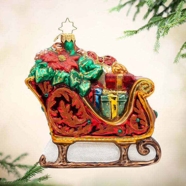 Rustic Regal Ride. Ornament of Santa's bright red and golden sleigh carrying multiple different colored presents. View of front