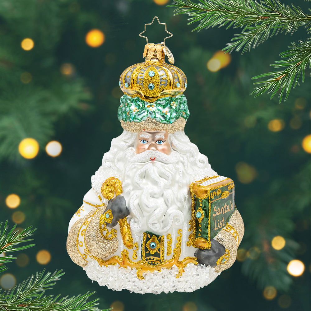 Ivory Majesty. Ornament of Santa in a shimmering gold robe, and a golden crown. With a glittering cane in one hand a Nice List in the other. View of front.