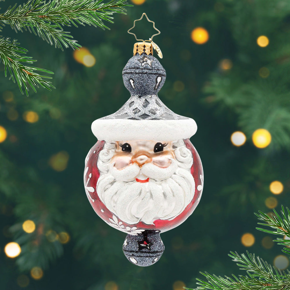 Jolly Snowflake Sparkle. A round ornament in red with Santa's face in the front and a black and silver bell on top and on the bottom. View of front.