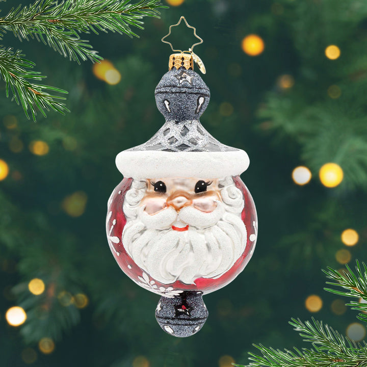 Jolly Snowflake Sparkle. A round ornament in red with Santa's face in the front and a black and silver bell on top and on the bottom. View of front.