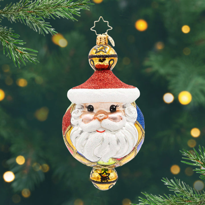 Joyful Jingles. A round ornament of red, blue and gold with Santa's face on the front and a bell at the top and on the bottom. View of front.