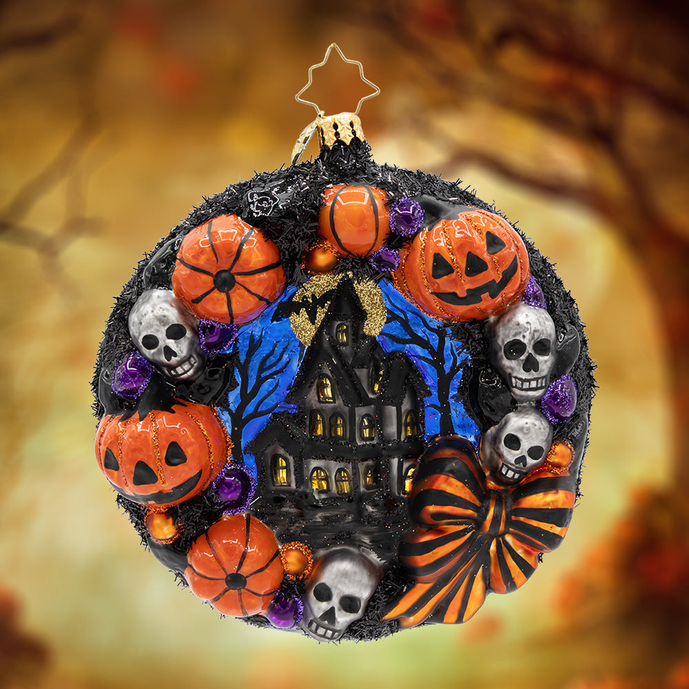 Wicked Welcome Wreath. This wreath ornament, in a haunting black color with the smiling pumpkins, ghostly skulls, and a hand-painted scene of a house in the center. View of the front.