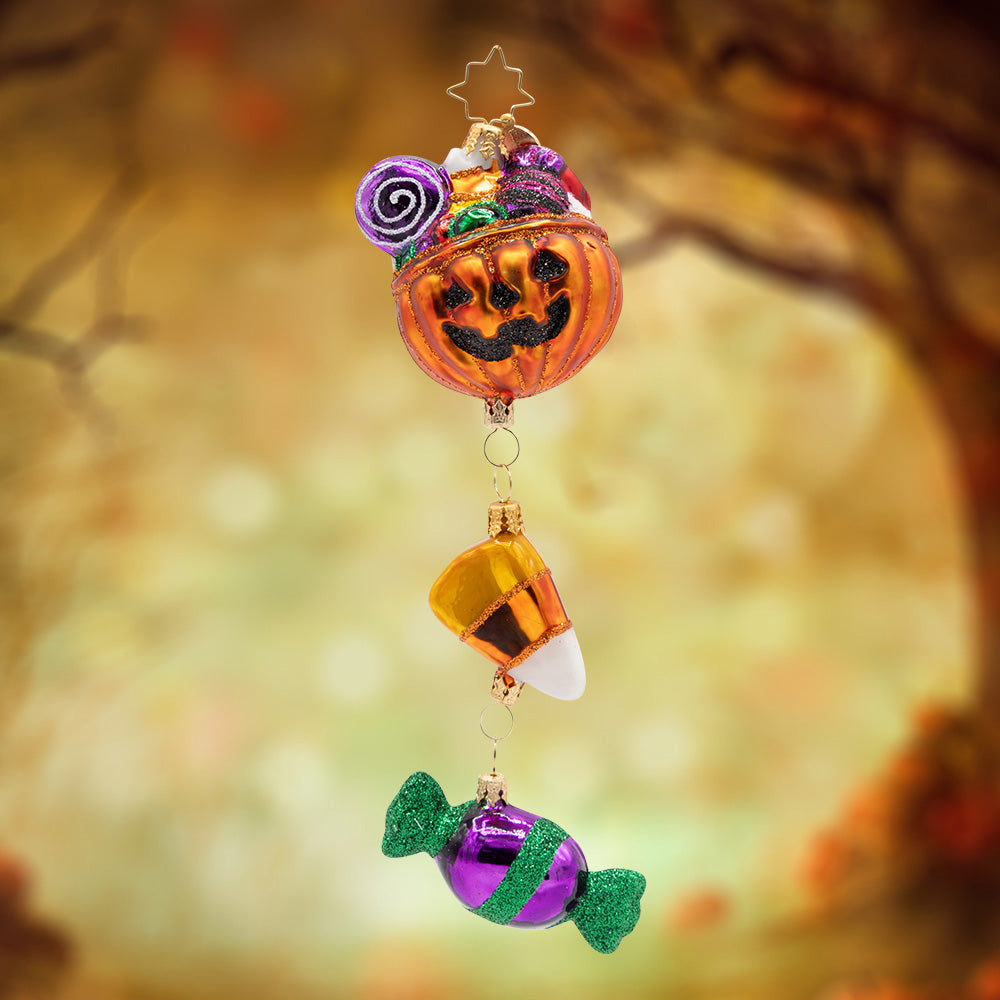 Trick or Treat Trio. This ornament consist of a bright orange pumpkin holding candy corn which is holding a purple candy. View of front