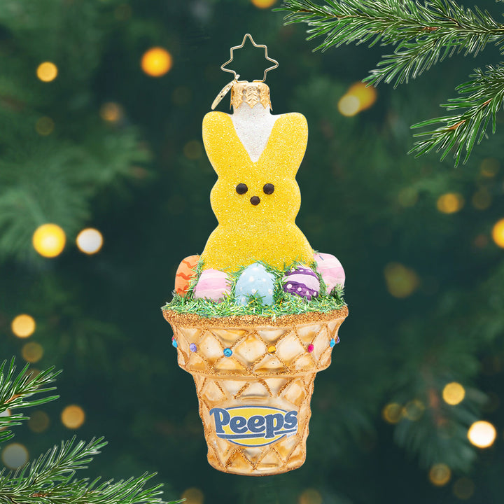 A Sweet PEEPS® Treat. A yellow peep bunny ornament surrounded by different easter eggs inside of a golden waffle cone. View of front