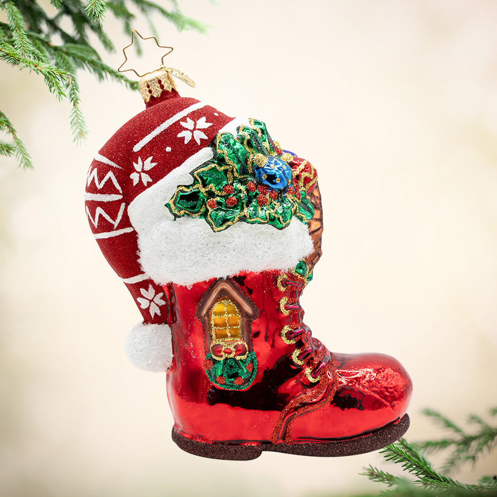 The Jolly Boot Inn. A shiny red ornament shaped like a boot with a gold window, mistle, and a Santa hat on top. View of front