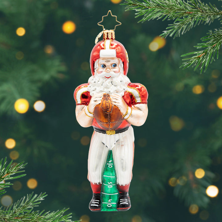 North Pole MVP. Ornament of Santa dressed in a red and white football uniform while holding a football. View of front