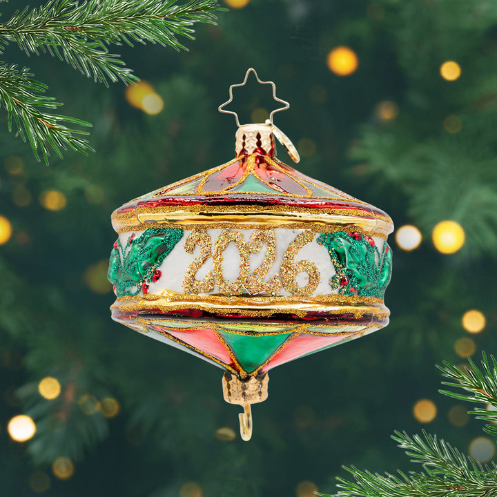 Remembering the Year 2026. ornament. Festive shades of green and red, sprigs of holly, and dated "2025." View of front. 