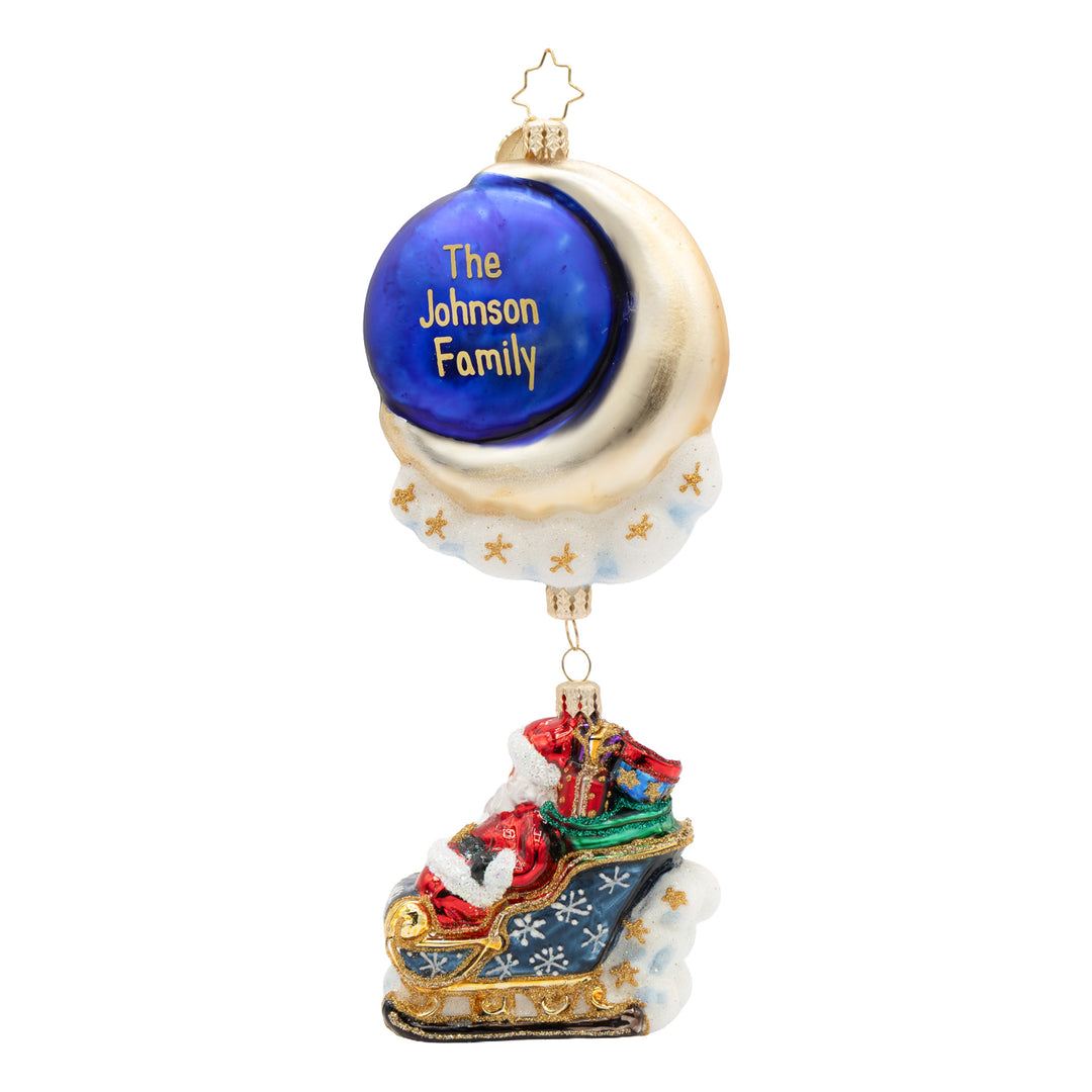 A personalized Christmas ornament featuring a gold crescent moon with a blue circle that reads 'The Johnson Family' in gold lettering, with Santa Claus sleighing in a decorated blue sleigh below, on a white background.
