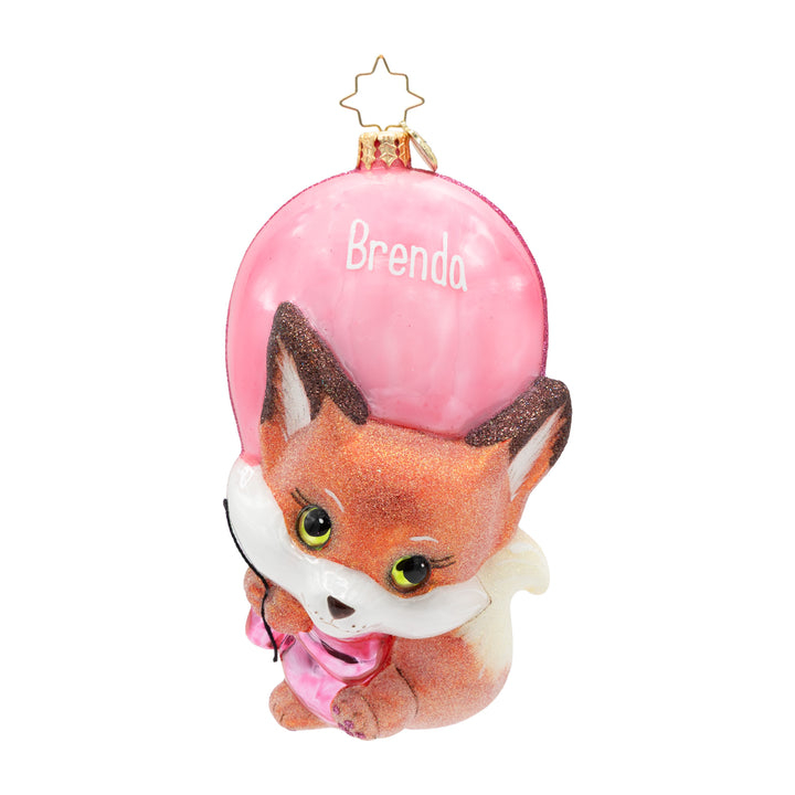 A personalized Christmas ornament featuring a cute cartoon fox wearing a pink scarf, holding a large pink balloon with the name 'Brenda' written on it, and a gold star hanging loop at the top.