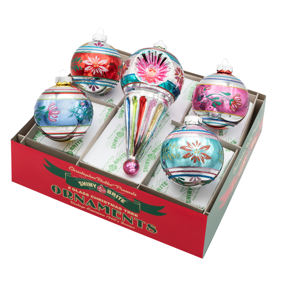 CHRISTMAS CONFETTI 5 COUNT 3.25” DECORATED ROUNDS & 7” SHAPE. Four silver round ornaments with stripes and designs in colors of red, blue, pink, and teal, along with a big round with a cone shape at the bottom in the same colors.