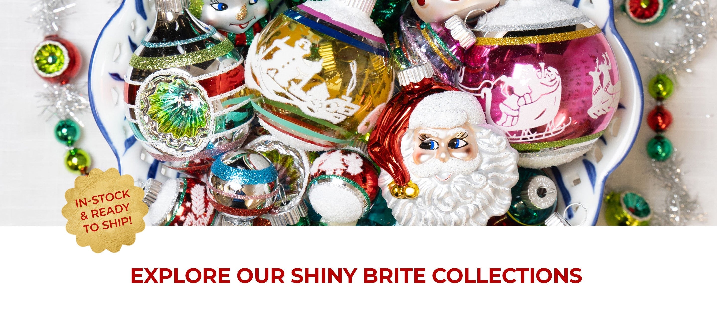 A colorful collection of vintage-style Shiny Brite Christmas ornaments piled in a decorative bowl, featuring Santa, snowman, and character figurines alongside glittery glass balls in red, green, gold, and pink.
