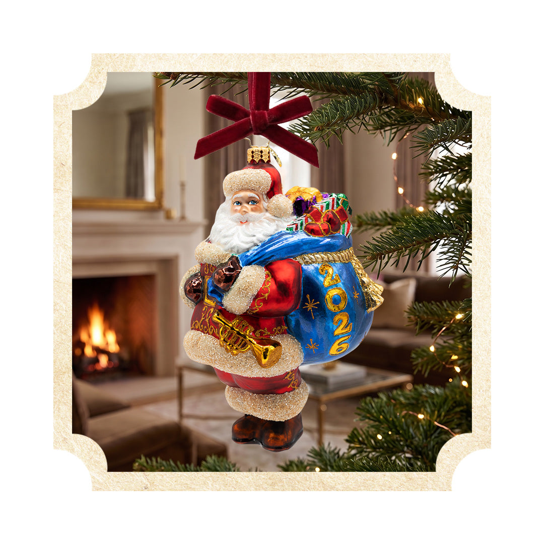 Dated 2026 Santa Claus glass Christmas ornament with a blue toy bag hanging on a tree.