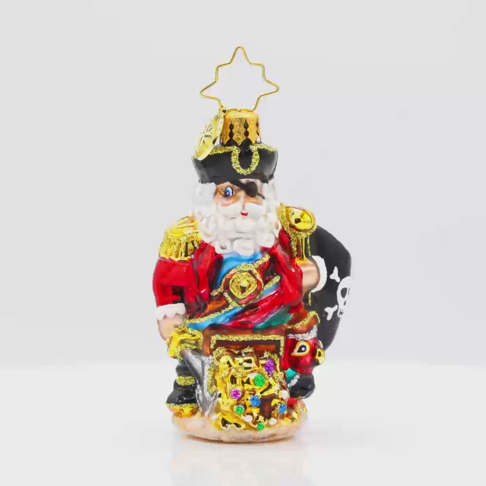 Swashbuckler Santa Gem ornament. Santa is dressed as a pirate, captains coat and eyepatch included. He sits atop a treasure chest with a pirate's flag in hand. View of back.