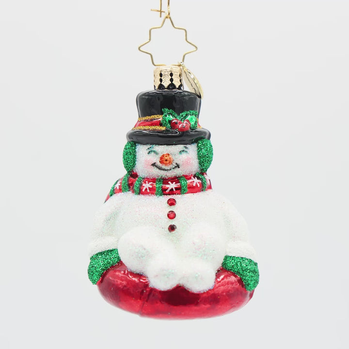 Front view of a snowman ornament wearing a red and green scarf on a red sled.