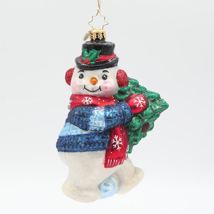 Front view of a decorative Christmas ornament shaped like a snowman holding a small tree, wearing a blue sweater and red mittens.