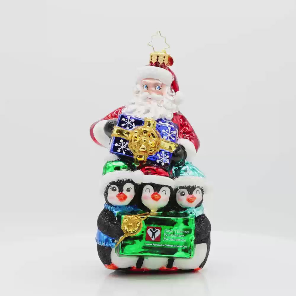 Santa Flurry Friends ornament. Santa is standing with three penguins in front of him, holding a gift with the Dave Thomas Foundation for Adoption logo on the front of it. Video.