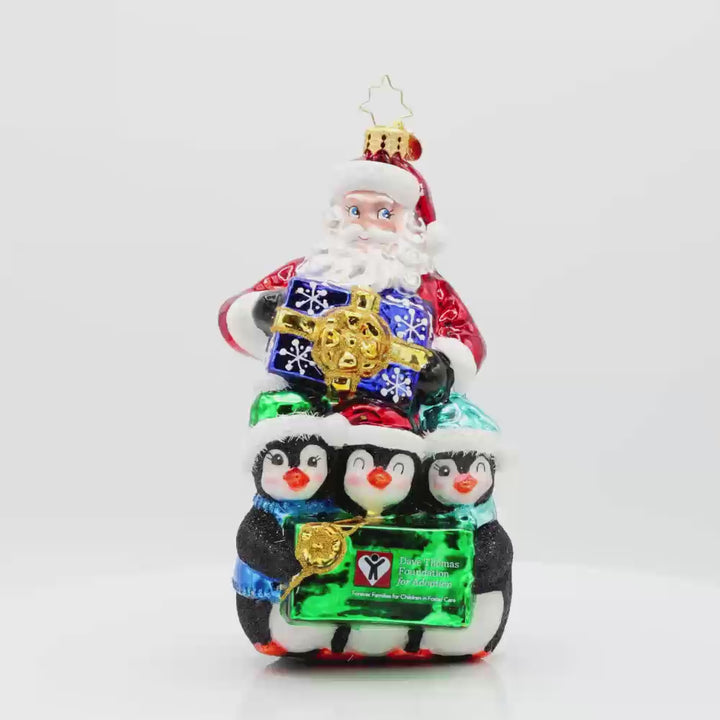 Santa Flurry Friends ornament. Santa is standing with three penguins in front of him, holding a gift with the Dave Thomas Foundation for Adoption logo on the front of it. Video.