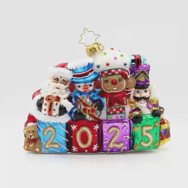 Stacking Up The Cheer ornament. A row of gifts dated with "2025." Behind them sits a snowman, gingerbread man, nutcracker and drummer boy. Video.
