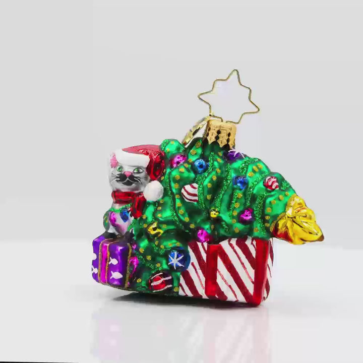 Festive Feline Fiasco Gem ornament. A grey cat sits on top of a present next to a half-fallen decorated Christmas tree. Video.