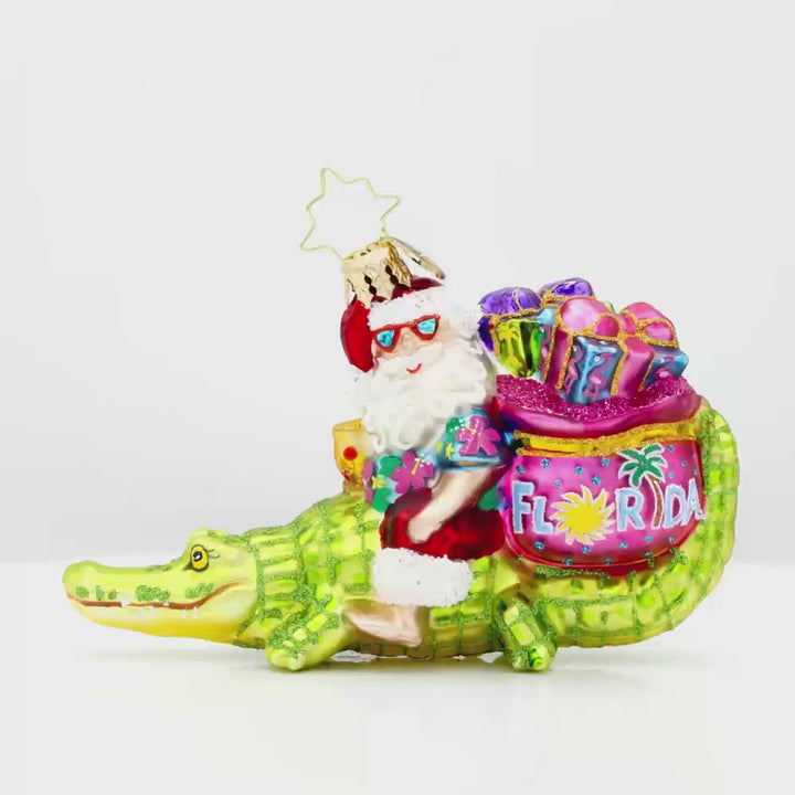 Sunshine State Gator ornament. Santa is trading in his sleigh for a gator and enjoying a tropical cocktail. "Florida" is written on gift sack. Video.