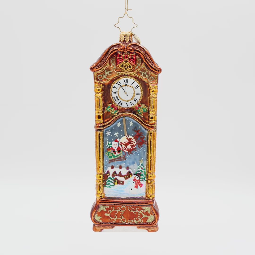 Front view of a gold and brown grandfather clock ornament with a scene of Santa arriving to town in his sleigh.